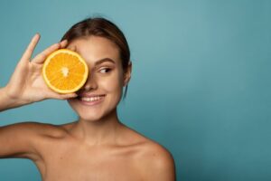 caucasian female with clean skin laughing with closed eyes and showing half of fresh orange while advertising benefits of vitamin C